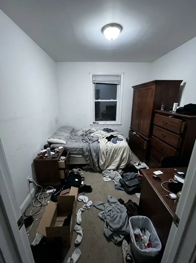 Small bedroom with clutter, harsh lighting, and poor furniture arrangement.